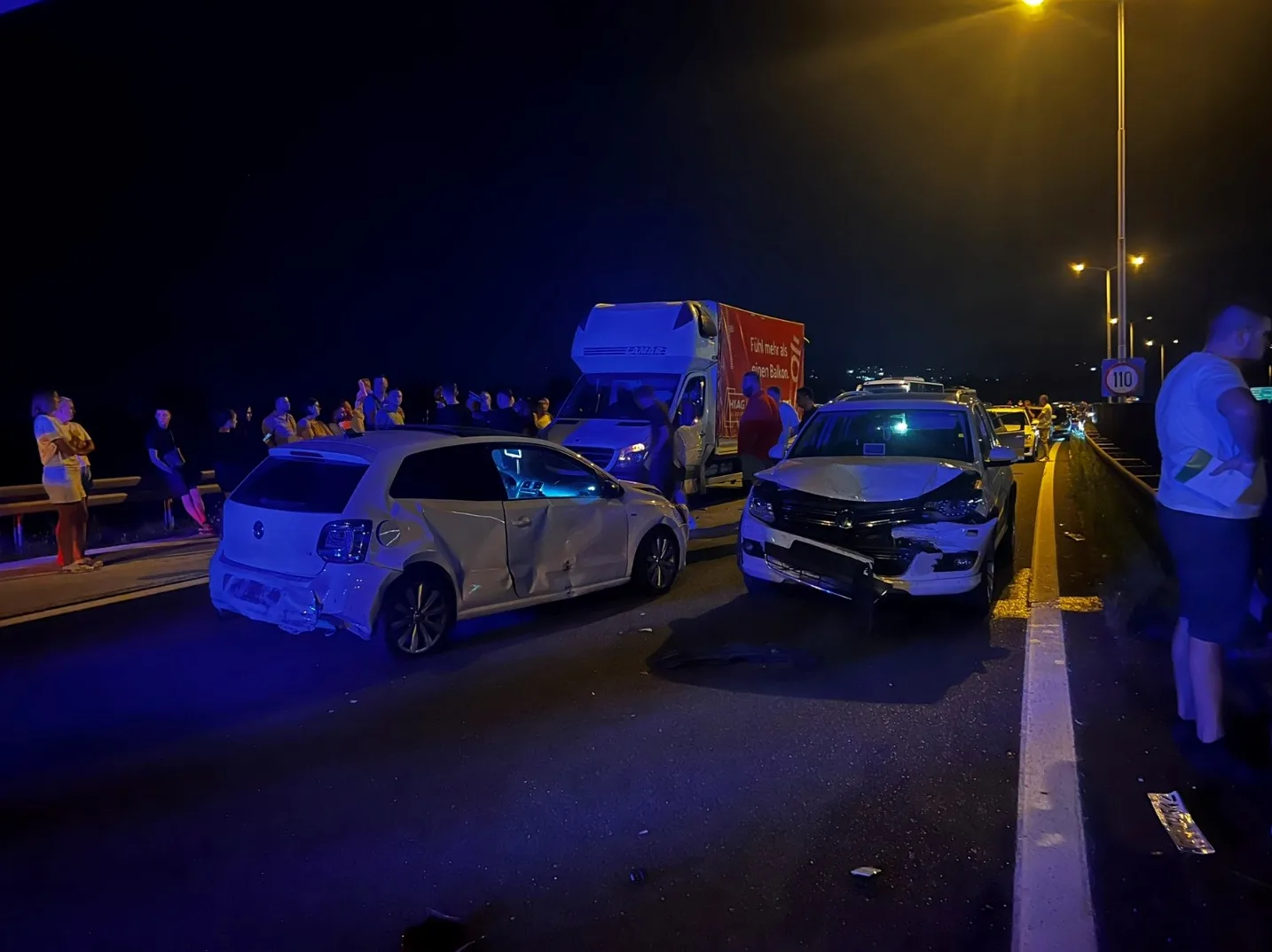 Udes dva automobila i kamiona na autoputu noću, sa okupljenim ljudima pored puta.