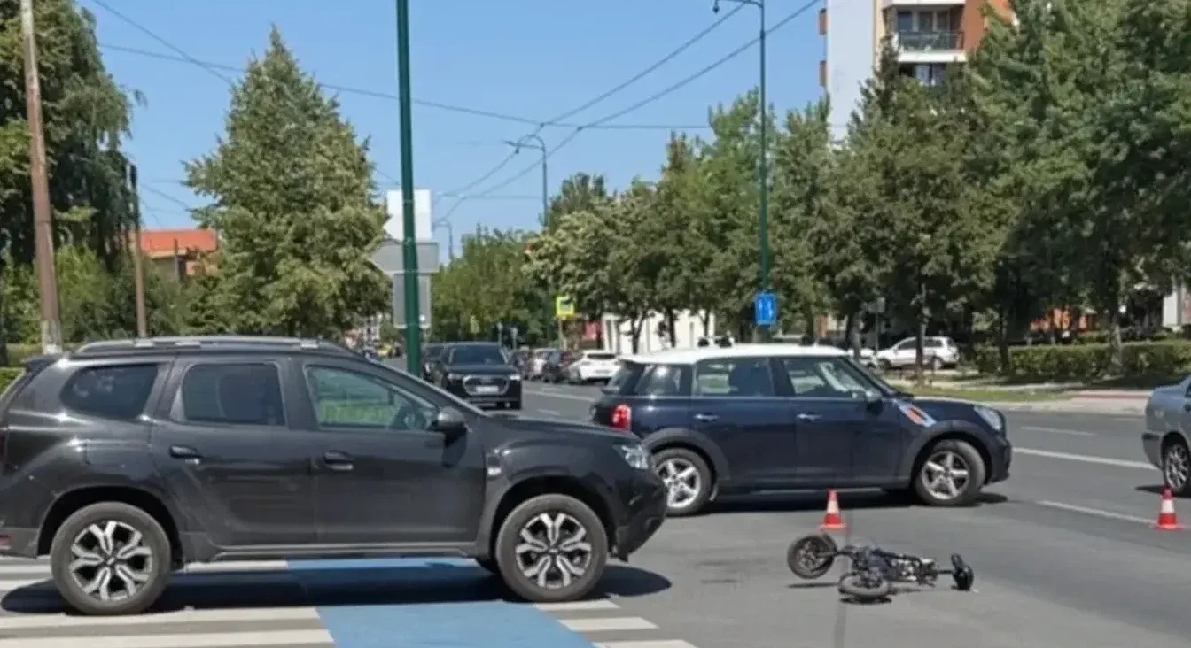 Saobraćajna nesreća sa palim električnim trotinetom na pješačkom prijelazu, pored tamnog SUV-a i tamnoplavog automobila