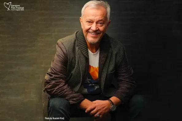 Portret osunčanog gospodina sa sijedom kosom i bradom, odjevenog u jaknu preko majice, nasmijanog i opuštenog.