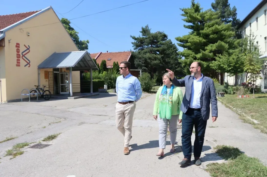 Tri osobe, dva muškarca i jedna žena, hodaju po asfaltnom putu ispred zgrade sa natpisom "ingeb".