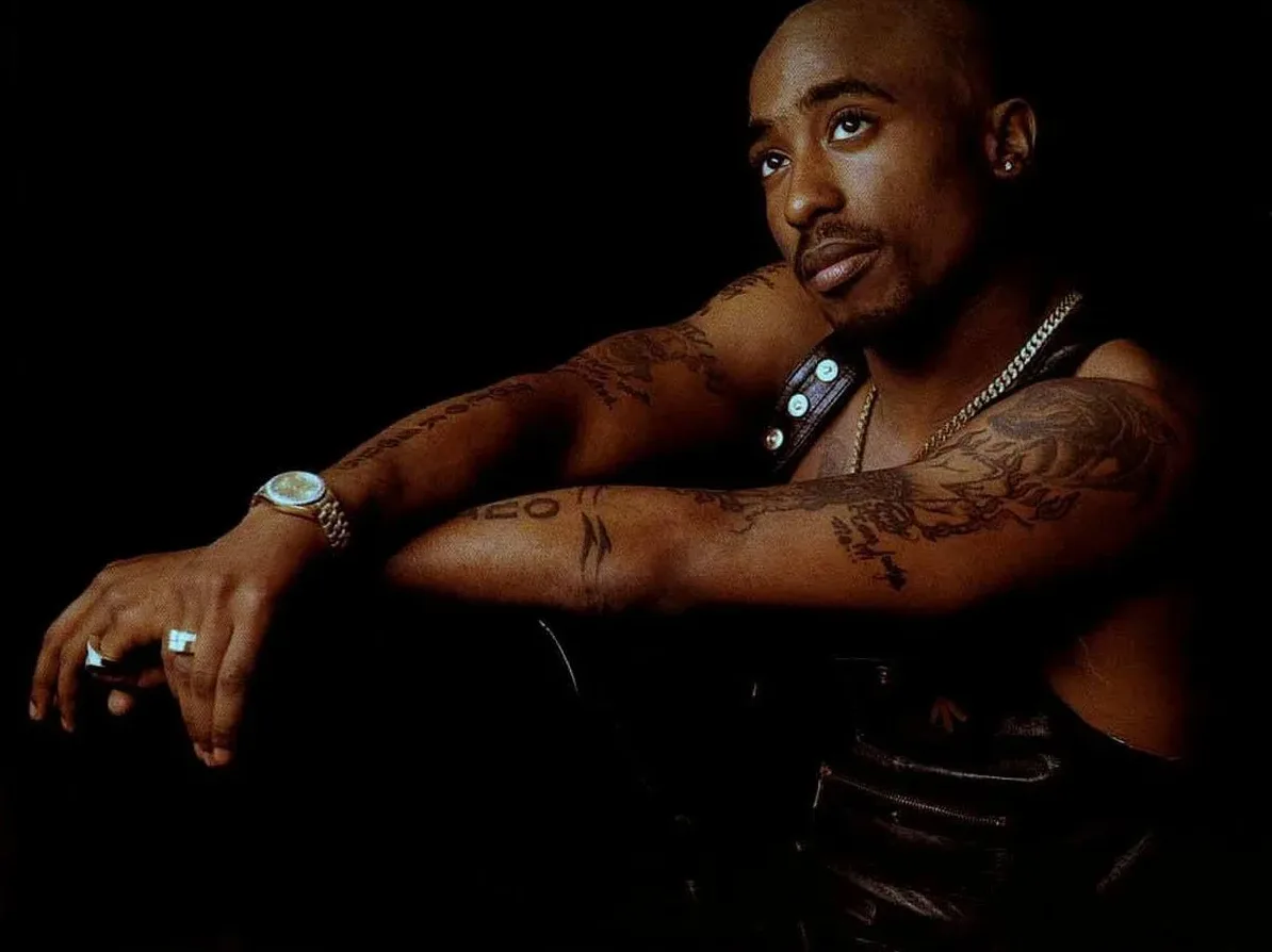 Portret repera Tupaca Shakura sa tetovažama na rukama i zlatnim nakitom.
