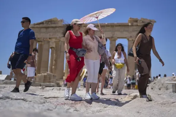 Grupa turista posjećuje drevne ruine Akropolja u Grčkoj, uživajući u sunčanom danu dok razgledaju istorijska mjesta.