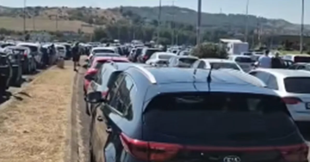 Veliko parkiralište sa nizovima parkiranih automobila, gdje se vidi nekoliko osoba, vjerovatno na javnom događaju ili lokaciji sa velikom posjećenošću.