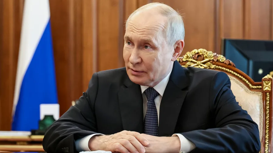 Vladimir Putin u svečanom odijelu sjedi za stolom ispred zastave Rusije.