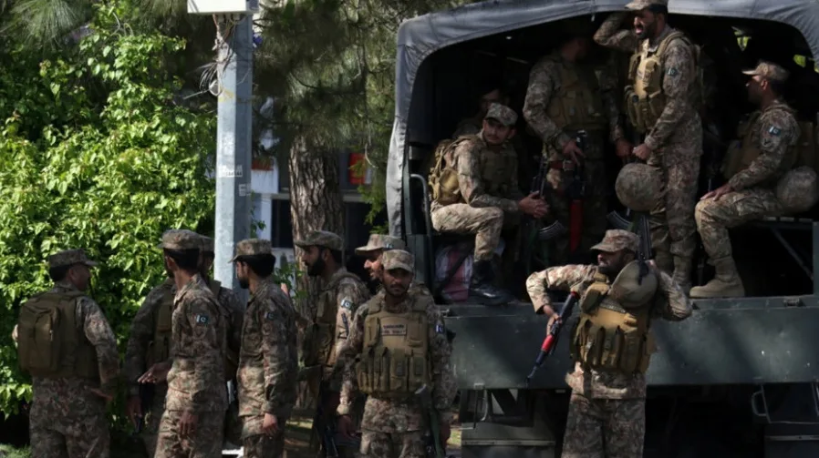 Pakistanaski vojnici u punoj opremi, sa automatskim puškama, stoje i sjede u i oko vojnog kamioneta na ulici, uz drveće i zgrade u pozadini.