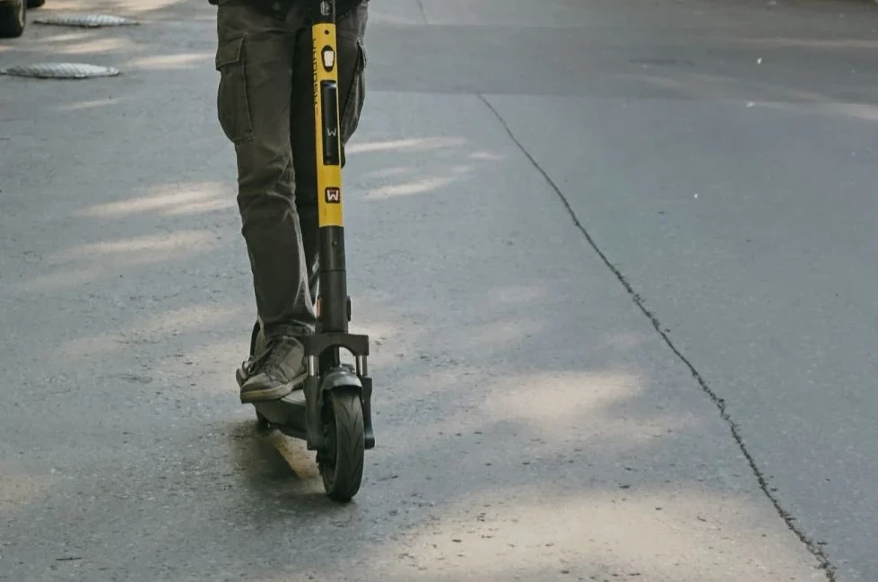 Osoba vozi električni romobil žute boje po asfaltiranom putu.