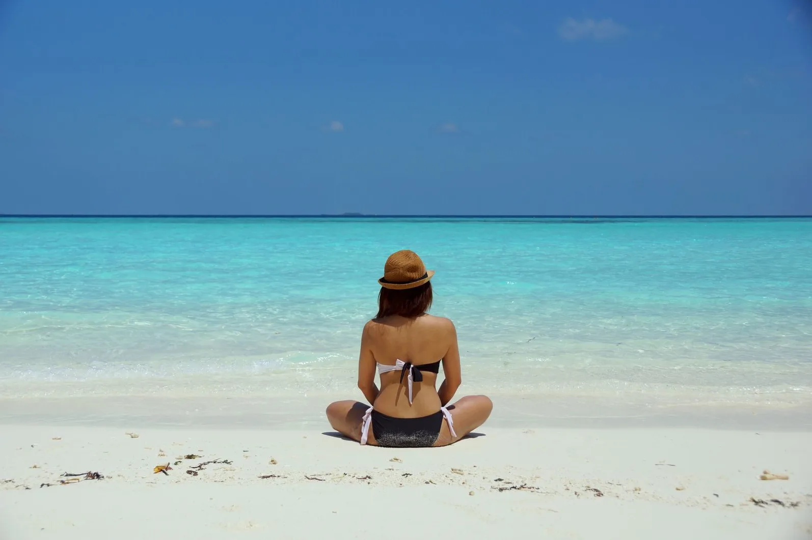 Rear view of a woman in a bikini and hat relaxing on a pristine beach in Maldives.